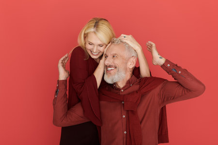 A joyful senior couple laughs and shares love in stylish outfits against a vibrant backdrop.