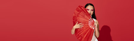 A stylish young asian woman displays her creativity with striking eye makeup while posing with a fan, bannerの写真素材