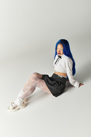 Stylish young woman sits gracefully, showcasing her unique blue hair and fashionable ensemble.の写真素材