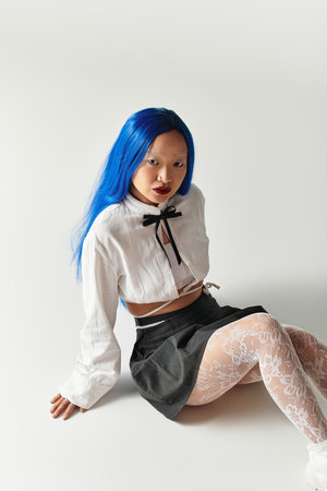 A young woman with blue hair showcases her trendy outfit and unique beauty in a grey studio.の写真素材