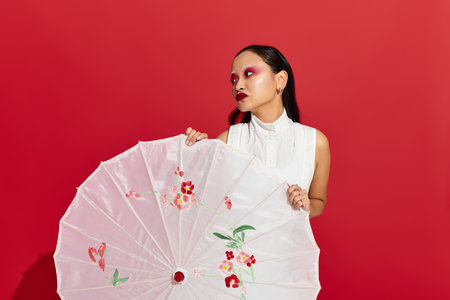 A confident young asian woman poses with a parasol, flaunting vibrant makeup and a stylish outfit.の写真素材