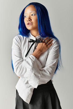 A confident young woman with blue hair showcases her stylish outfit in a grey studio.の写真素材