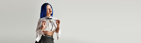 Young woman in a fashionable outfit poses in a grey studio with blue hair, bannerの写真素材