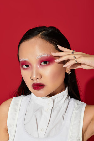 A stylish young asian woman showcases bold eye makeup against a striking red backdrop.の写真素材