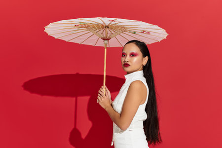 A confident young asian woman with a parasol flaunts her striking eye makeup and fashion.の写真素材