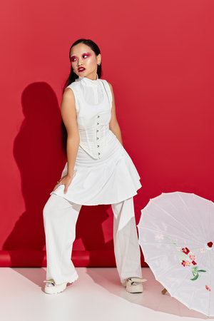 A young Asian woman confidently poses in a red studio, flaunting her stylish outfit and makeup.の写真素材