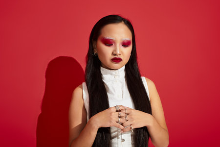 A confident young Asian woman shines in vivid makeup and a stylish outfit in a red studio.の写真素材