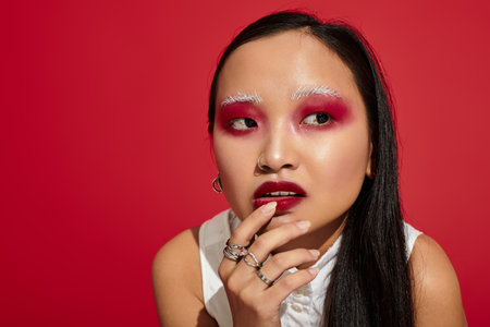 Young asian woman displays stunning eye makeup and stylish outfit against a bold backdrop.の写真素材