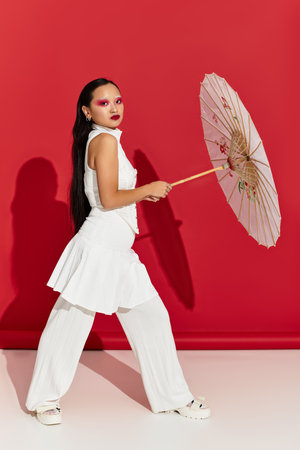 A stunning young asian woman confidently poses with a parasol, flaunting her vibrant eye makeup.の写真素材
