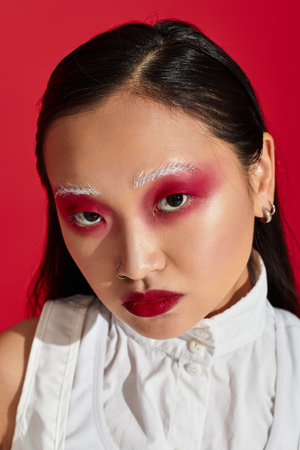 A striking young asian woman displays her artistic eye makeup and stylish outfit in a vivid studio.