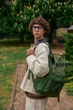 Handsome young student strolls through a tranquil outdoor setting with a backpack in hand.