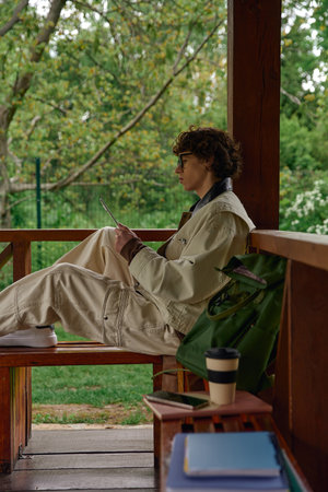 A young man in casual clothes sits on a bench, thoughtfully reviewing his notes in the greenery.の写真素材