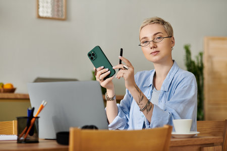 A young woman with short hair is focused on her work at home, holding a phone and a pen.の写真素材