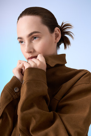 Young beautiful woman radiates style while posing gracefully in a trendy brown jacket.