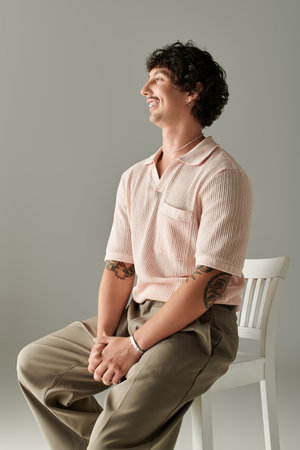 Stylish young man poses confidently on a chair, showcasing his fashionable outfit and charisma.