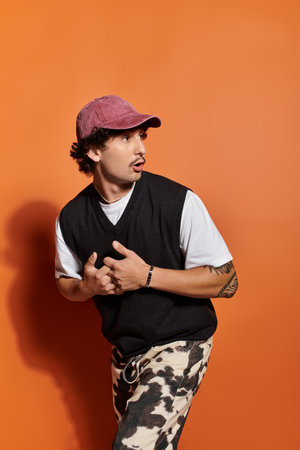 A stylish young man in trendy attire stands confidently against a vibrant orange backdrop.