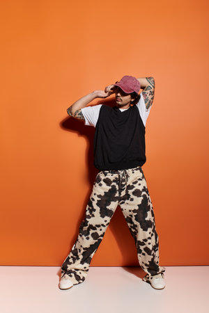 A stylish young man poses casually in trendy streetwear against an artistic backdrop.
