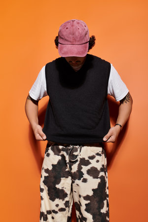 A handsome man adjusts his trendy outfit while standing in front of an eye catching orange wall.