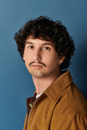 A stylish young man with curly hair and a mustache exudes confidence.