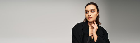 A young woman in a chic black ensemble poses gracefully in a sophisticated studio setting, banner