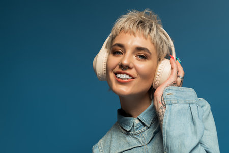 Beautiful young woman smiles while wearing headphones, surrounded by a vibrant blue backdrop.のeditorial素材