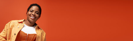 A confident plus size African American woman models a chic autumn outfit against orange backdrop,...