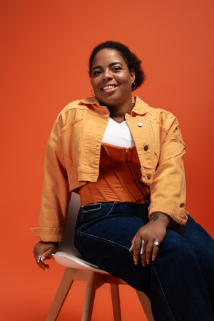 A stylish plus-size Black woman poses confidently in an autumn outfit against a vibrant backdrop.