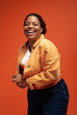 A plus size African American woman showcases her autumn fashion with confidence and joy in a studio.