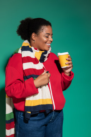 Brightly dressed woman radiates joy while holding a warm drink in a studio setting.