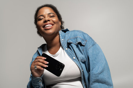 A plus-size Black woman flaunts a stylish autumn outfit, smiling and holding her phone.