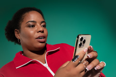 A stylish plus-size Black woman in a vibrant studio checks her phone in a trendy autumn outfit.