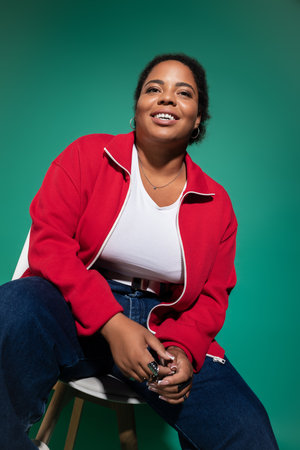 Plus size african american woman smiles confidently in a trendy autumn outfit inside a studio.