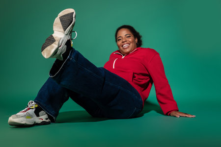 A plus size African American woman wears a chic autumn outfit, enjoying vibrant studio vibes.