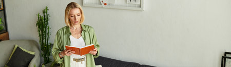 Woman stands in her cozy living room, immersed in reading a book while dressed in casual attire.
