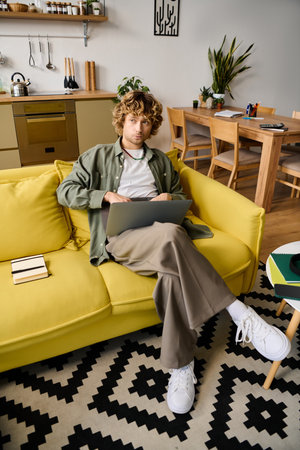 Casual man sits comfortably on a vibrant yellow couch, focused on his laptop in a cozy room.