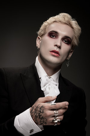 Handsome man poses in elegant Halloween disguise, highlighting dark makeup and unique attire.