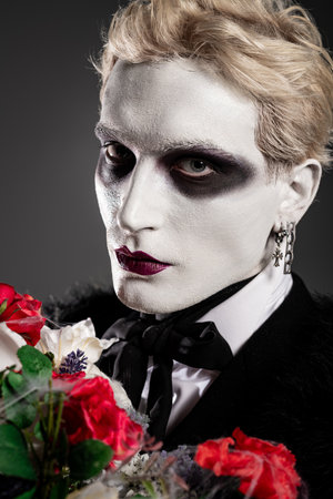 Young man in a detailed Halloween costume poses with roses, flaunting his makeup and style.の写真素材