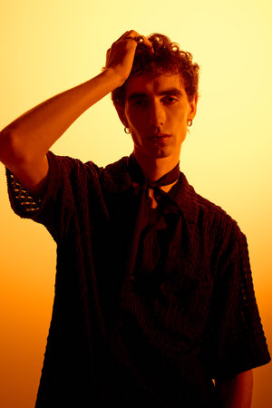 A handsome young man poses confidently in fashionable attire while the sunset glows behind him.のeditorial素材