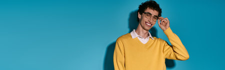 A young man in a yellow sweater and glasses stands confidently, showcasing his charming style.