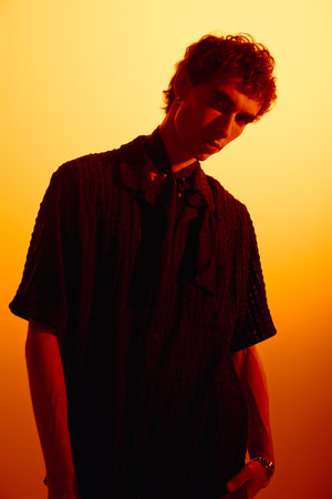 Handsome young man showcases modern fashion while standing in front of a warm orange backdrop.のeditorial素材