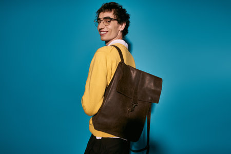 A stylish young man smiles, wearing a trendy outfit and backpack.