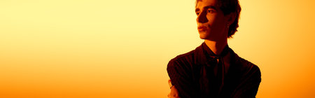 A young man dressed in fashionable attire stands confidently, surrounded by warm sunset hues.