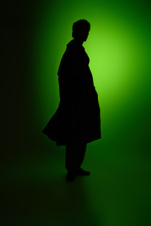 A fashionable young man strikes a pose, his silhouette highlighted by a striking green light.の写真素材