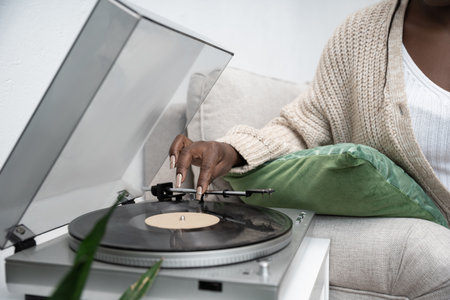An African American woman in a cardigan plays vinyl records in her modern living room.の写真素材