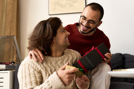 A joyful couple exchanges gifts in their cozy living room, embracing the holiday spirit.の写真素材