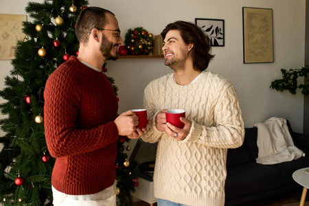 Two loving men share joyful moments together, holding red mugs in a festive home setting.