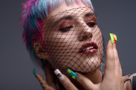 A young woman showcases her unique style with short, colorful hair and artistic nails in a studio.