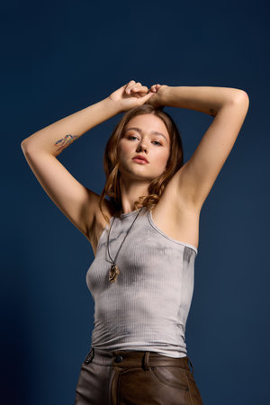 Pretty young woman poses confidently in a brown leather outfit against a blue studio backdrop.