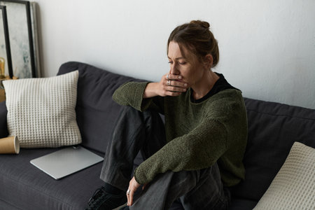 In a quiet moment at home, a young woman reflects on her emotions while seated on a couch.