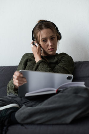 Struggling with her emotions, a young woman sits quietly on the couch, lost in thought and music.